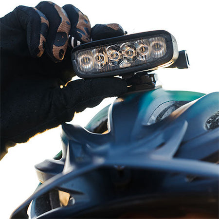 Gloved hand pressing the button on a Hangover bike helmet light mounted on a helmet
