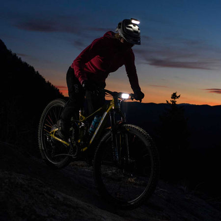 Mountain biker riding at twilight with a handlebar bike light and helmet light switched on
